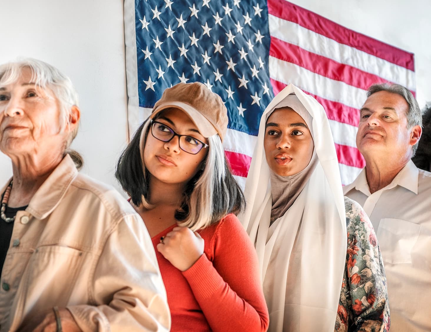 People of different ages and backgrounds waiting together beneath an American flag